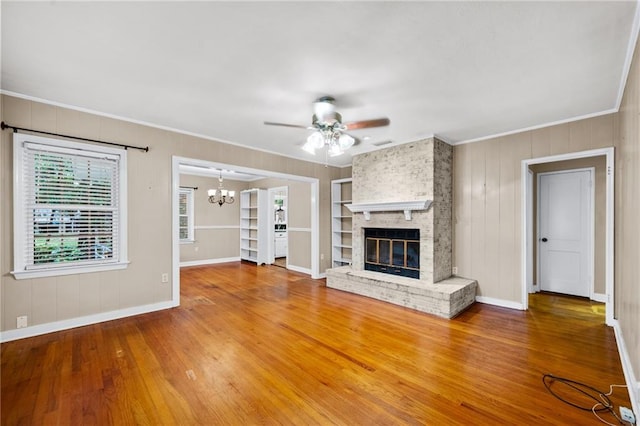 unfurnished living room featuring built in features, hardwood / wood-style floors, ceiling fan with notable chandelier, a brick fireplace, and ornamental molding