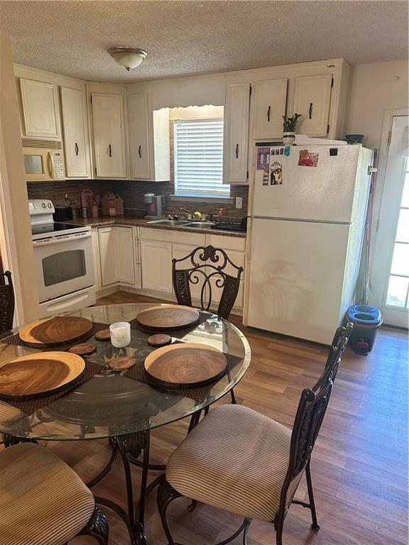 kitchen featuring a sink, white appliances, wood finished floors, and white cabinets