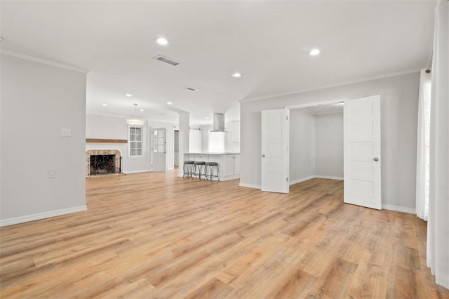 unfurnished living room featuring light wood-style floors, crown molding, a fireplace, and visible vents