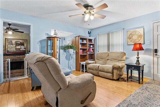 living room with ceiling fan, a brick fireplace, and light hardwood / wood-style floors