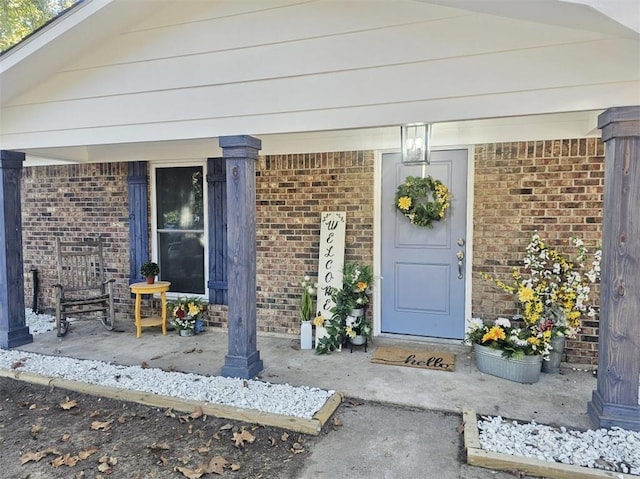 view of exterior entry featuring covered porch and brick siding