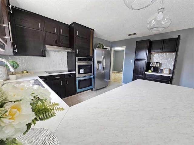 kitchen with light countertops, decorative backsplash, appliances with stainless steel finishes, a sink, and under cabinet range hood