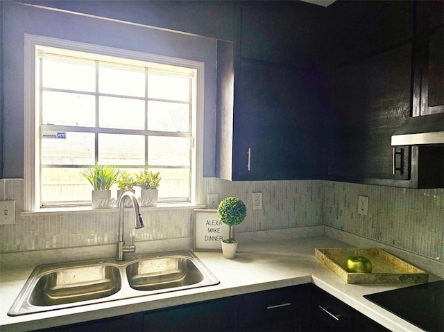 kitchen featuring black electric stovetop, tasteful backsplash, light countertops, a sink, and wall chimney range hood