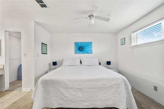 bedroom with ceiling fan, a textured ceiling, a closet, a spacious closet, and light colored carpet