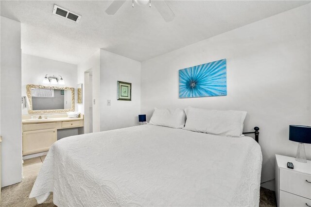 bedroom featuring ceiling fan, light colored carpet, ensuite bathroom, and sink