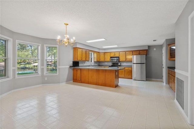 kitchen featuring a notable chandelier, a textured ceiling, brown cabinetry, stainless steel appliances, and a peninsula