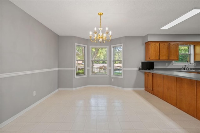 kitchen with an inviting chandelier, baseboards, brown cabinets, a sink, and decorative light fixtures