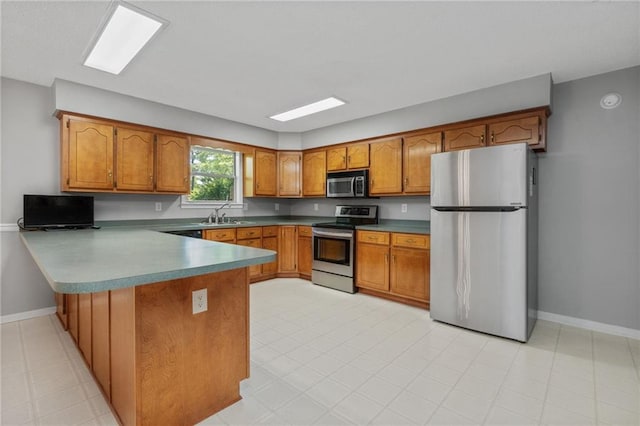 kitchen featuring brown cabinets, a peninsula, appliances with stainless steel finishes, and a sink