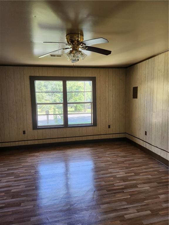 spare room with dark wood-type flooring, ceiling fan, and wooden walls