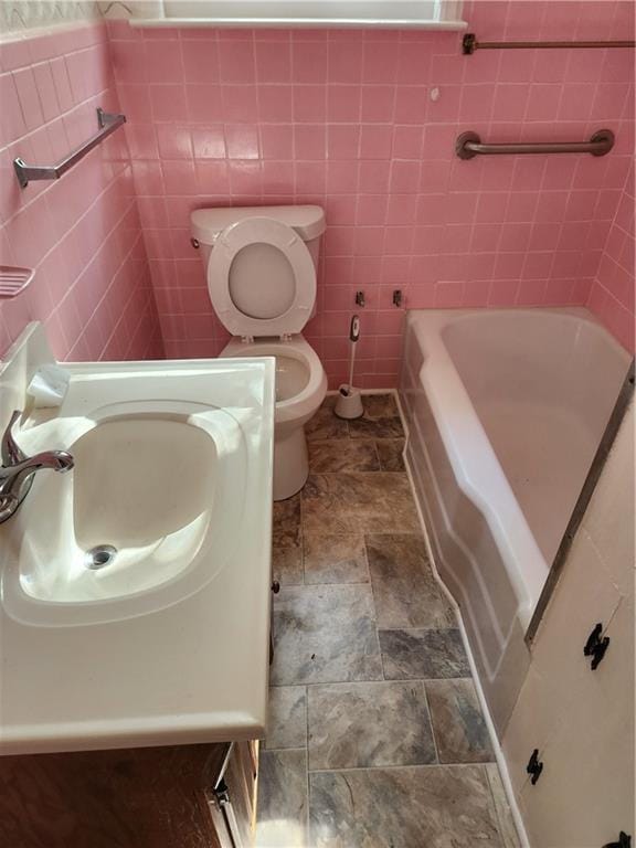 bathroom featuring vanity, toilet, tile walls, and a washtub