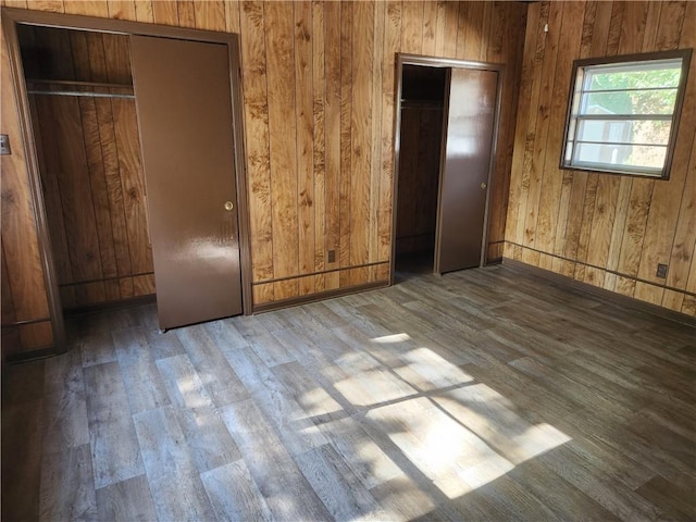 unfurnished bedroom featuring two closets, wood walls, and wood-type flooring