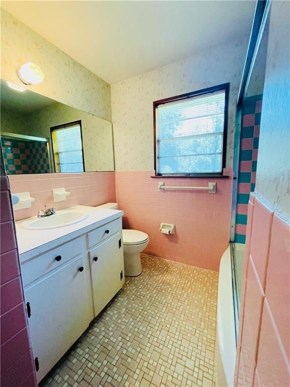 full bathroom with shower / bath combination with glass door, vanity, toilet, and tile walls