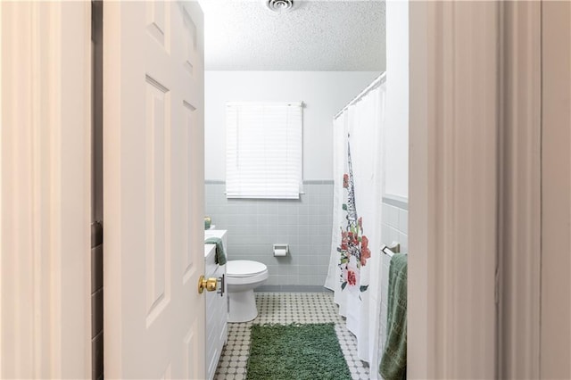 bathroom with vanity, a textured ceiling, tile walls, tile patterned flooring, and toilet