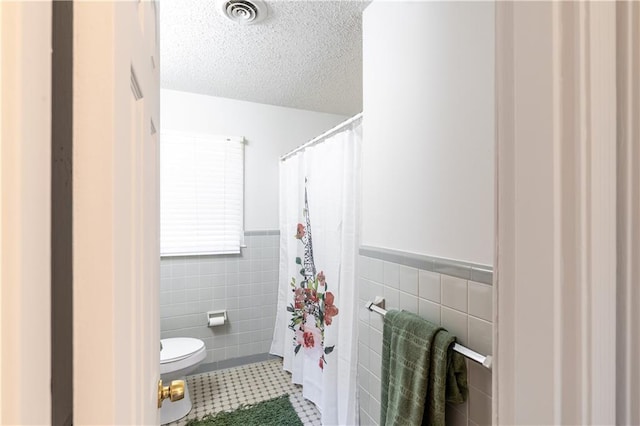 bathroom with tile patterned floors, toilet, tile walls, and a textured ceiling