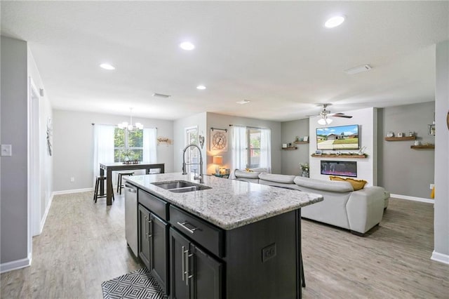 kitchen featuring a glass covered fireplace, a kitchen island with sink, a sink, light wood-type flooring, and dishwasher