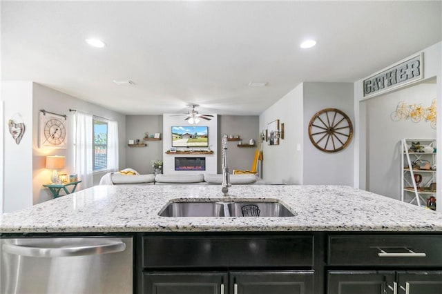 kitchen featuring a sink, open floor plan, dark cabinetry, dishwasher, and a glass covered fireplace