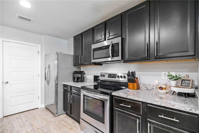 kitchen featuring visible vents, light wood-style floors, appliances with stainless steel finishes, dark cabinetry, and light stone countertops