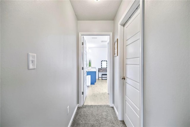 corridor with carpet, baseboards, and a textured ceiling