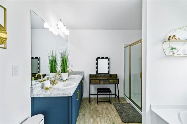 full bath with a stall shower, double vanity, a sink, and wood finished floors