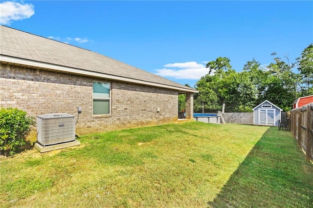 view of yard featuring a storage shed, a fenced in pool, a fenced backyard, an outbuilding, and cooling unit