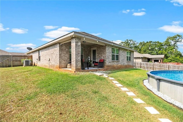 back of property with a fenced backyard, a fenced in pool, cooling unit, and a yard