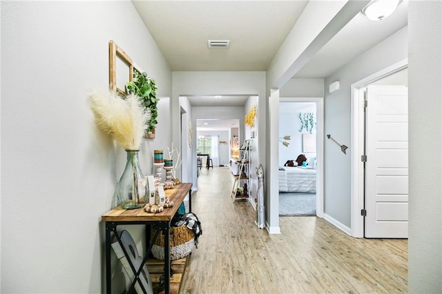 hallway featuring light wood-type flooring, visible vents, and baseboards