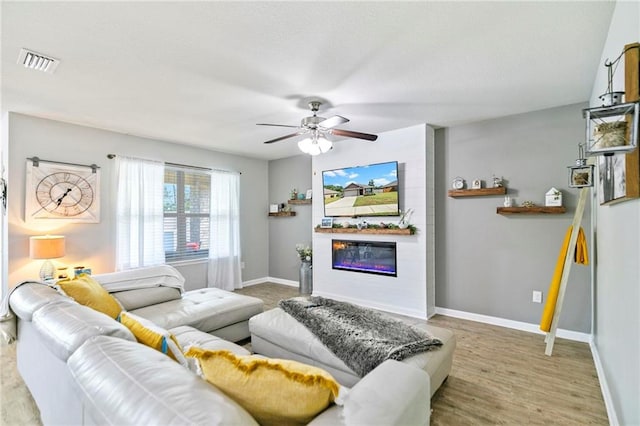 living room with wood finished floors, a ceiling fan, visible vents, baseboards, and a glass covered fireplace