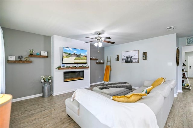 living room featuring a glass covered fireplace, visible vents, baseboards, and wood finished floors