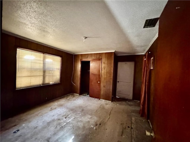 unfurnished bedroom with wood walls, a closet, and a textured ceiling