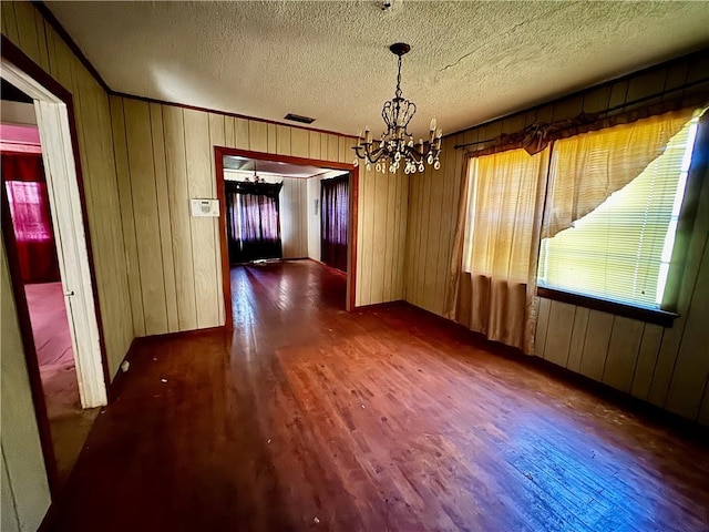 unfurnished dining area featuring a notable chandelier, a textured ceiling, visible vents, wood walls, and wood finished floors