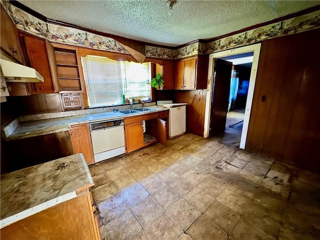 kitchen featuring a textured ceiling, under cabinet range hood, brown cabinetry, dishwasher, and a sink