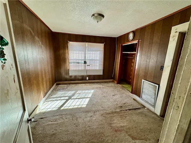 unfurnished bedroom with carpet, a textured ceiling, visible vents, and wood walls