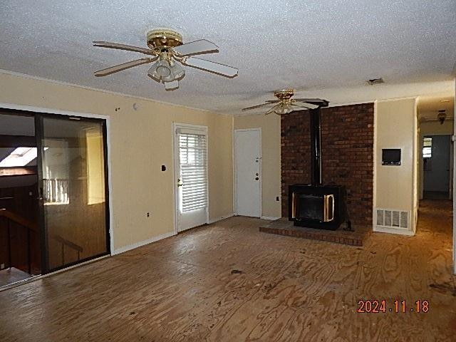 unfurnished living room with wood-type flooring, a textured ceiling, and a wood stove