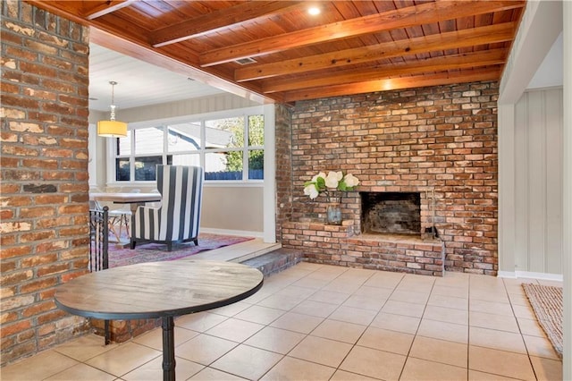 unfurnished living room featuring beamed ceiling, brick wall, a fireplace, light tile patterned floors, and wood ceiling