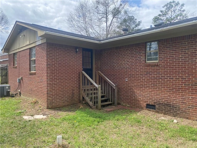 view of exterior entry featuring crawl space, brick siding, board and batten siding, and cooling unit