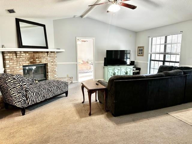 living area featuring visible vents, light carpet, lofted ceiling with beams, a fireplace, and ceiling fan