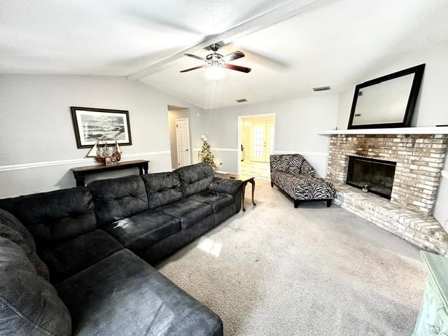 carpeted living room with a fireplace, vaulted ceiling with beams, and ceiling fan