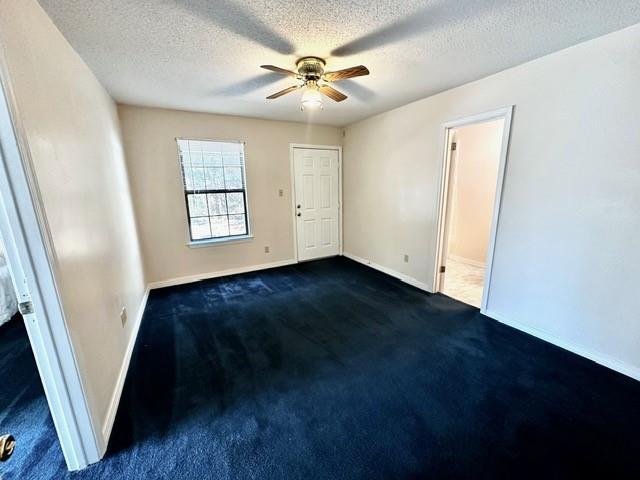 empty room with a textured ceiling, baseboards, dark colored carpet, and ceiling fan