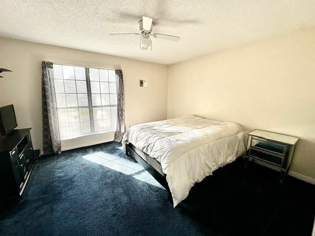 bedroom with a textured ceiling, a ceiling fan, and dark colored carpet