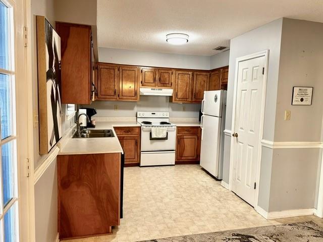 kitchen with white appliances, light floors, a sink, under cabinet range hood, and brown cabinets