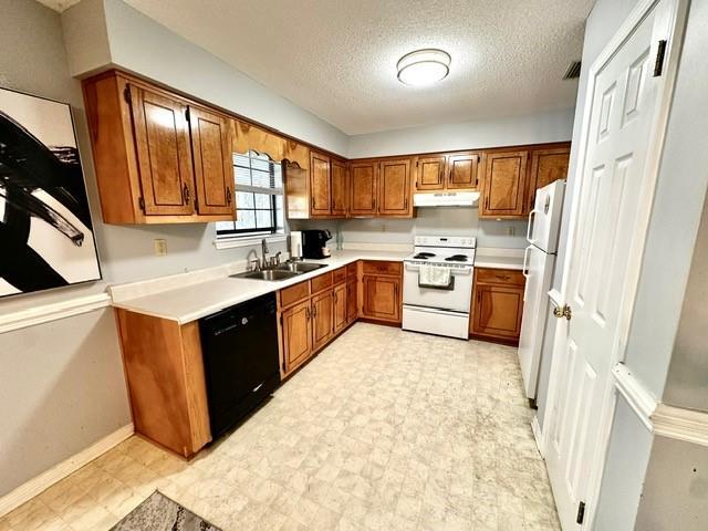 kitchen with white appliances, light floors, a sink, under cabinet range hood, and brown cabinets