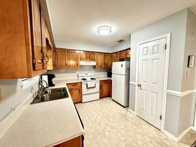 kitchen with visible vents, light floors, brown cabinets, white appliances, and a sink