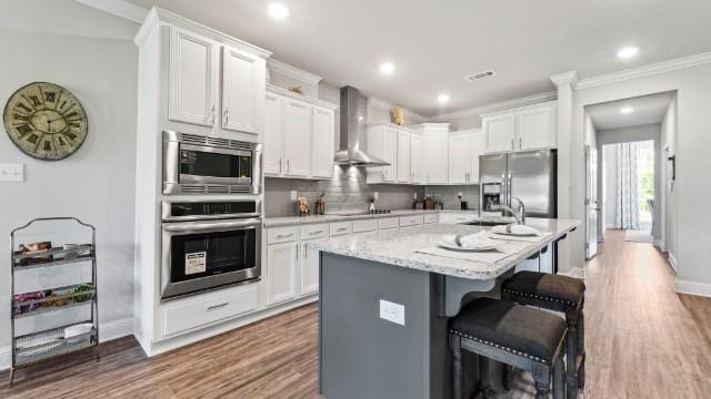 kitchen with wood finished floors, appliances with stainless steel finishes, white cabinetry, wall chimney exhaust hood, and backsplash