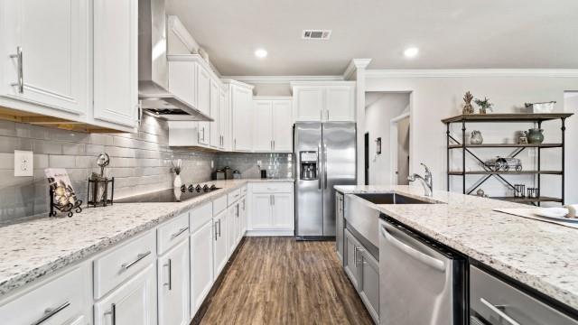 kitchen with dark wood-type flooring, backsplash, stainless steel appliances, wall chimney exhaust hood, and crown molding