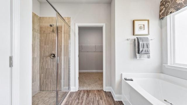 full bath featuring a walk in closet, baseboards, a stall shower, wood finished floors, and a bath