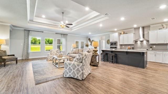 living room with crown molding, baseboards, ceiling fan, light wood-type flooring, and a raised ceiling