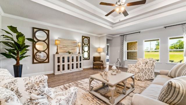 living area featuring a tray ceiling, wood finished floors, a ceiling fan, and ornamental molding