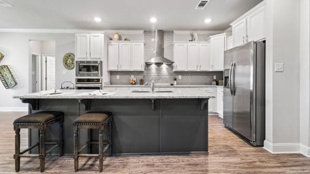 kitchen featuring white cabinetry, wall chimney exhaust hood, appliances with stainless steel finishes, and a sink