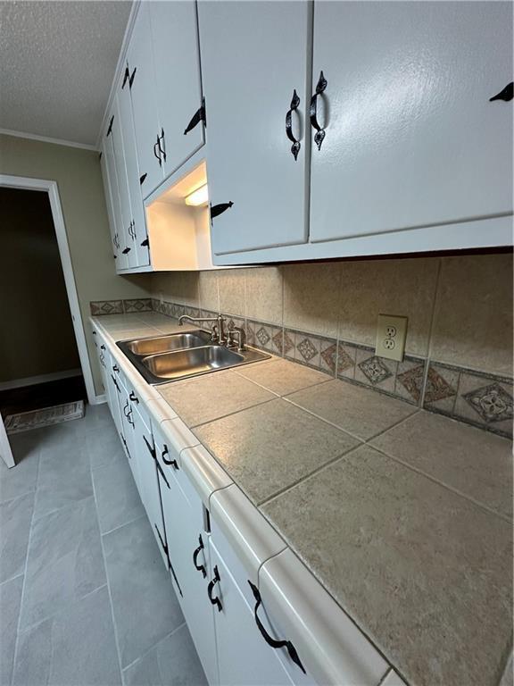 5405 Moffett Rd, Mobile, AL 36618 - kitchen featuring a textured ceiling, white cabinetry, decorative backsplash, crown molding, and a sink