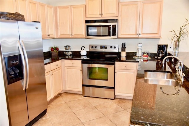 kitchen featuring light tile patterned floors, dark stone counters, stainless steel appliances, light brown cabinetry, and a sink